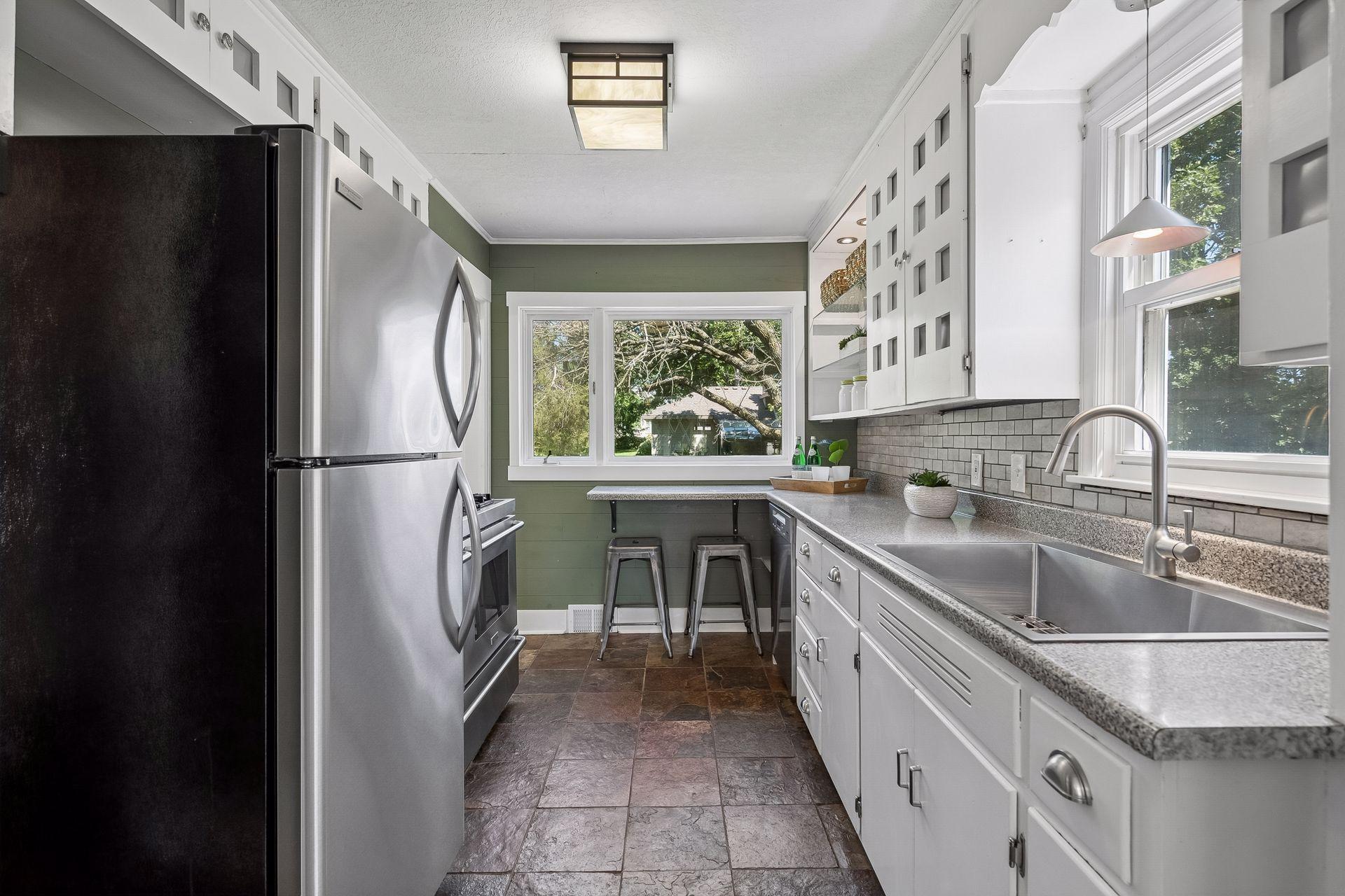 12x8 Main Floor Kitchen with White Cabinetry, Stainless appliances, lighted open shelving, and slate tile flooring. East and north-facing windows.