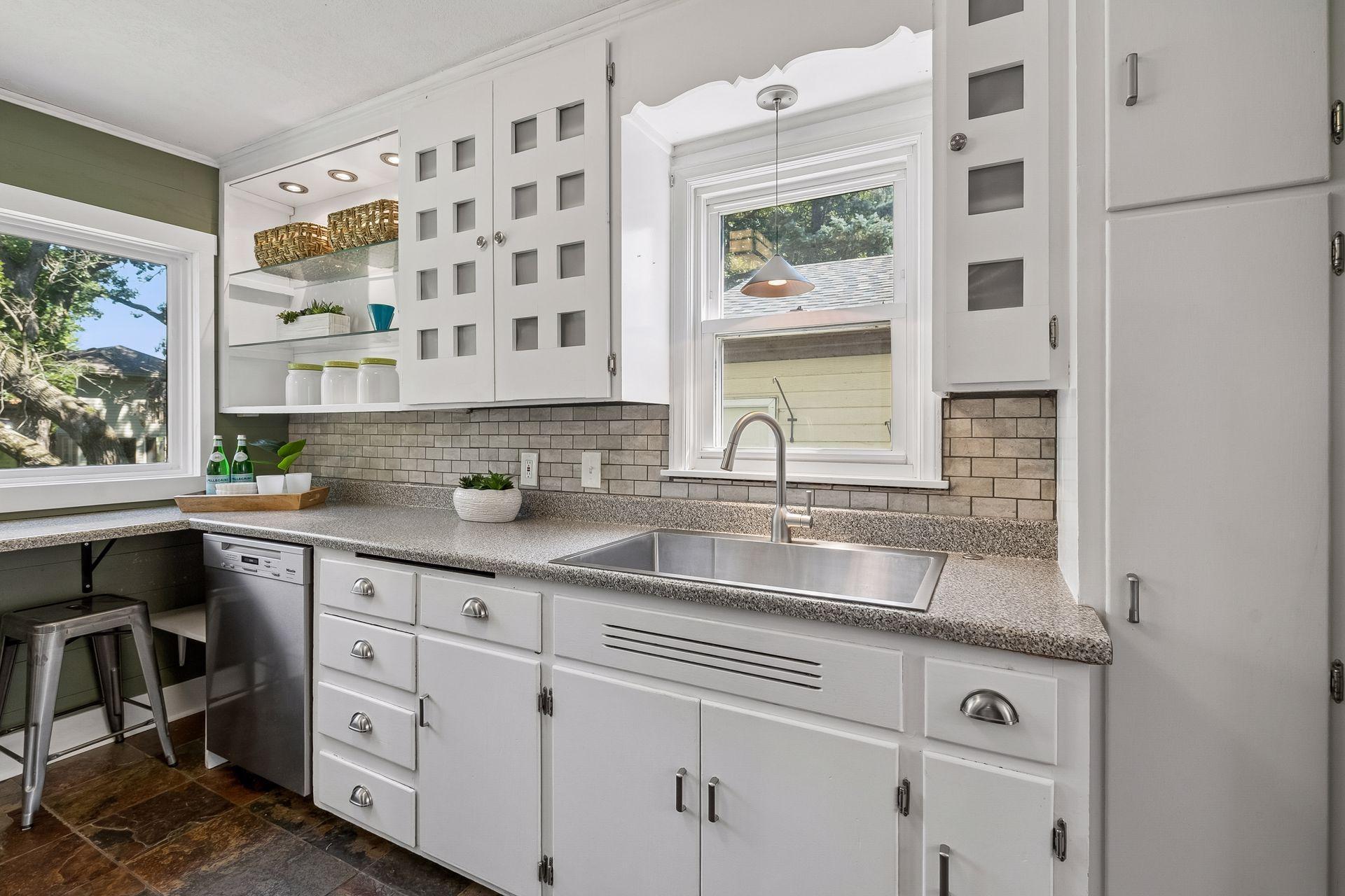 12x8 Main Floor Kitchen with White Cabinetry, Stainless appliances, lighted open shelving, and slate tile flooring. East and north-facing windows.