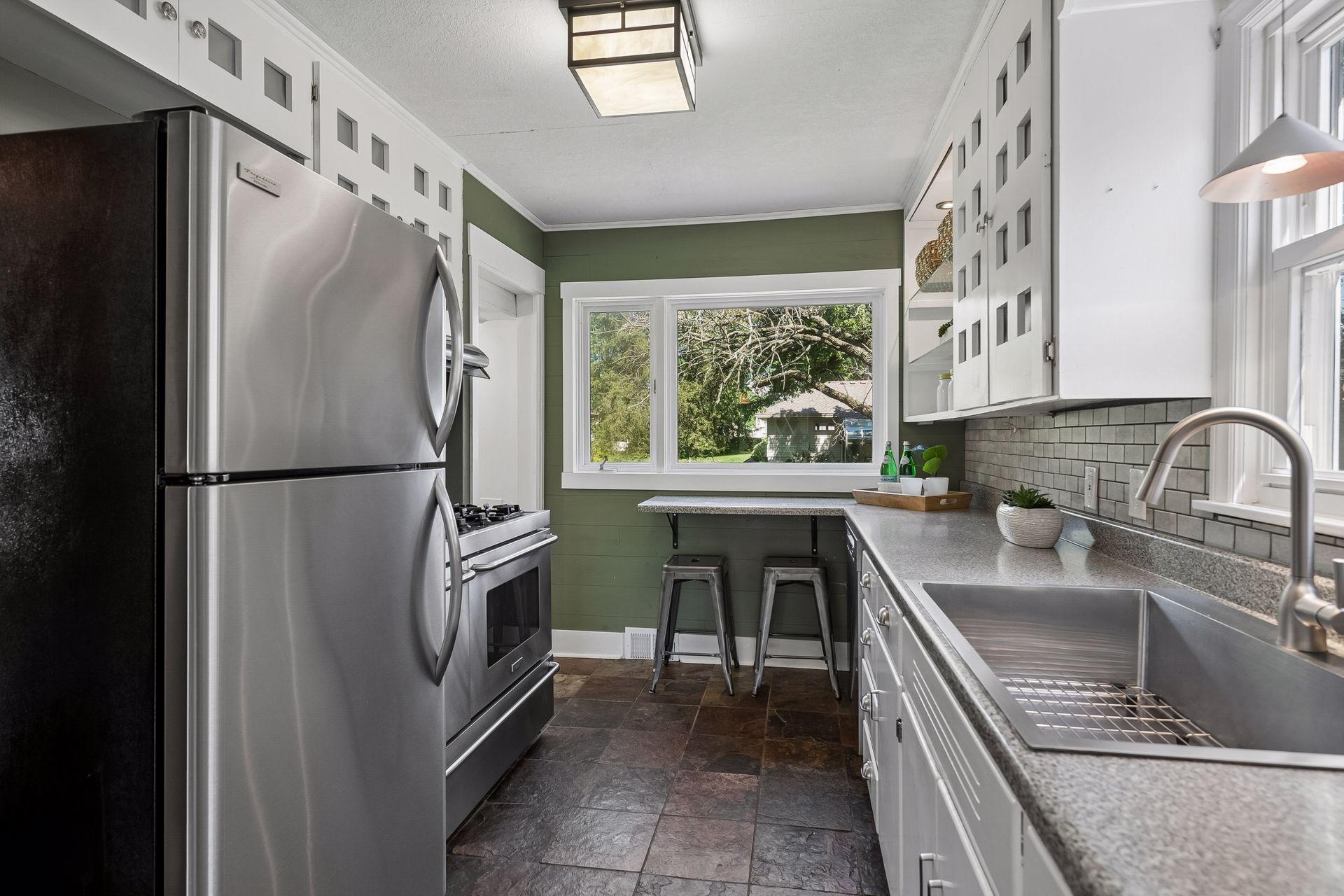 12x8 Main Floor Kitchen with White Cabinetry, Stainless appliances, lighted open shelving, and slate tile flooring. East and north-facing windows.