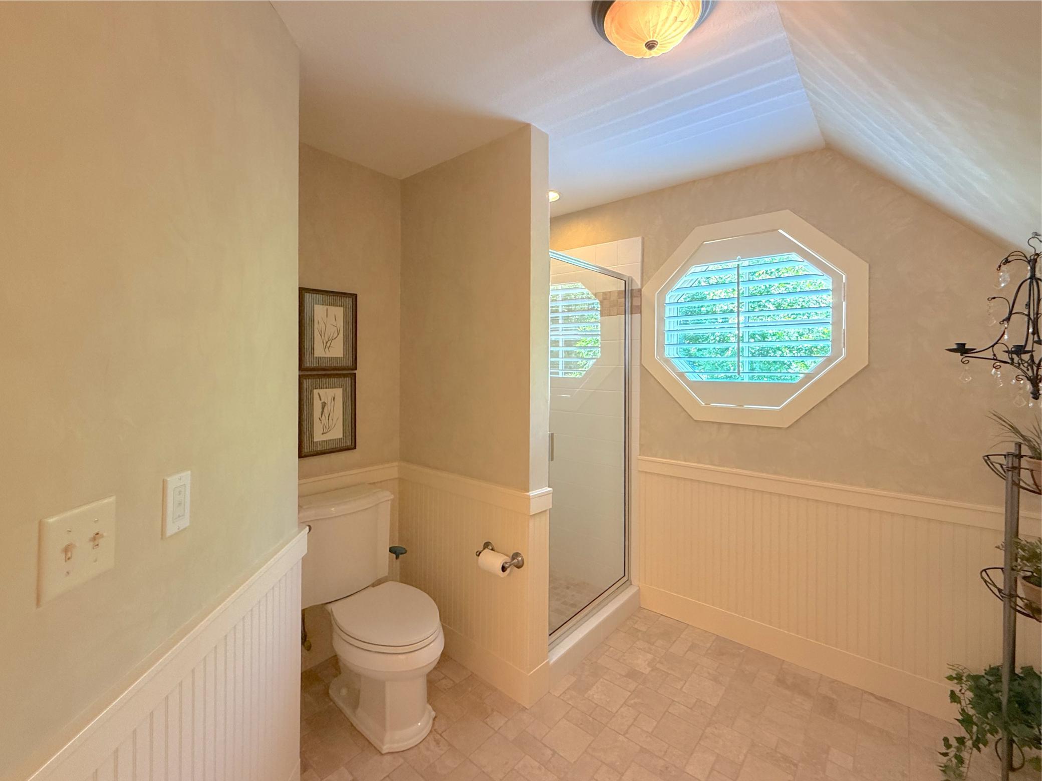 Another view of the 3-quarter bathroom offering interesting ceiling angles, tile flooring, wood wall accents and custom window.