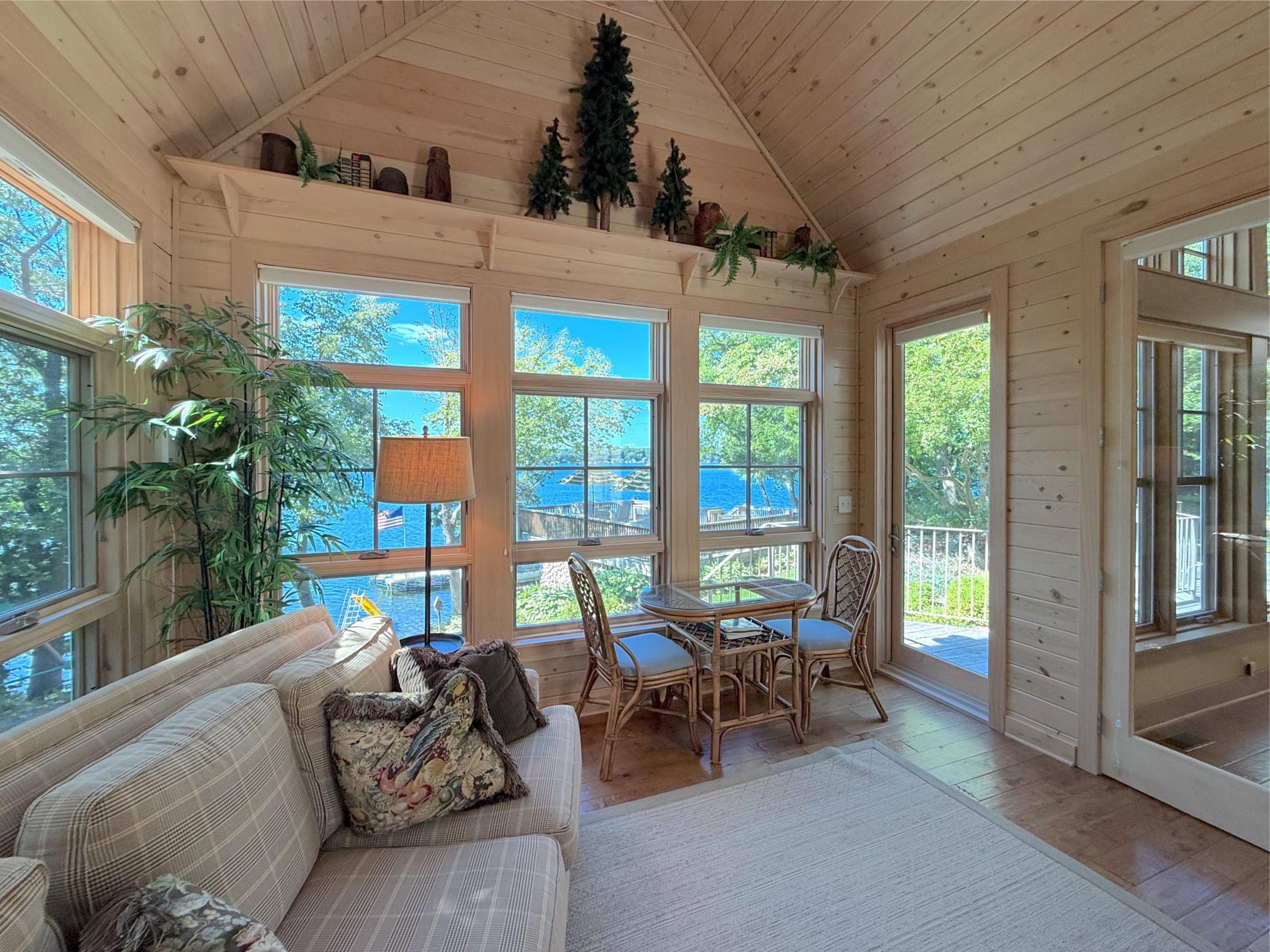 Cozy three-season porch wrapped in windows features a corner fireplace with brick and a lakeside wall of glass.