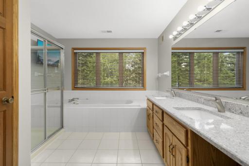 Primary bathroom with double sinks, separate tub & shower & views of backyard