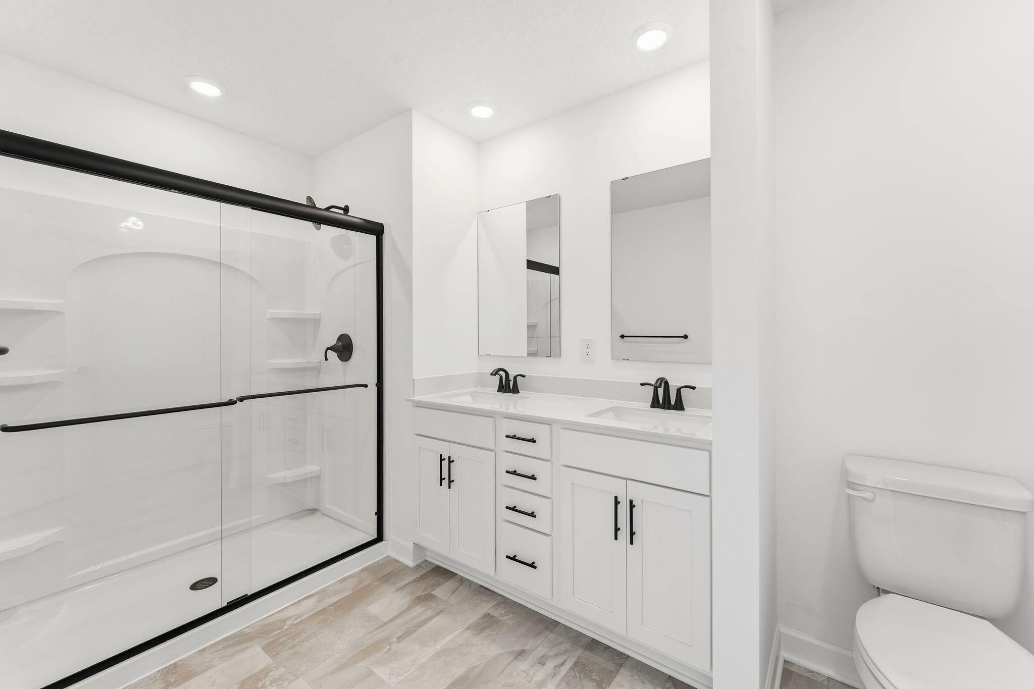 (Photo of a similar home, actual finishes may vary) Featuring a glass-enclosed shower with built-in shelving and glass mirrors set atop dual quartz sinks and vanity-cabinetry, the en-suite bathroom helps streamline morning routines
