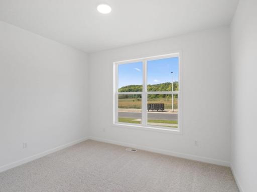 Overlooking the front of the home, this secondary bedroom enjoys natural light streaming in through its tall windows. It includes plush carpeting and a wardrobe closet.