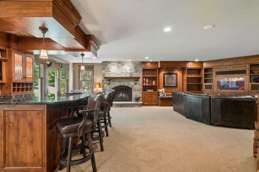 The lower-level family room features a stone gas fireplace, a large bar area, and a walkout to the backyard—creating an impressive and inviting entertaining space.