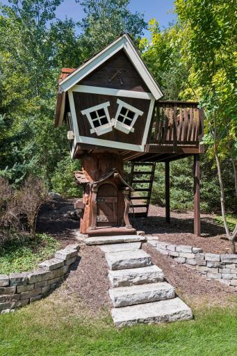 This charming, quirky treehouse features its own deck, offering a delightful backyard escape for kids or a whimsical touch to the landscape.