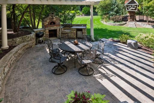 The patio overlooks lush green space and a charming treehouse/playhouse, creating a picturesque and inviting backyard setting.