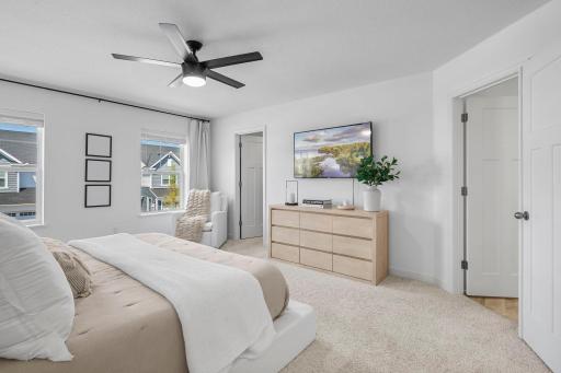 Large windows fill the primary bedroom with natural light, while the ceiling fan and fresh, neutral finishes add to the comfortable feel