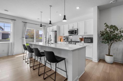 A kitchen you’ll love spending time in, featuring crisp white cabinetry, sleek countertops, stainless steel appliances, pendant lighting, and a generous center island with seating