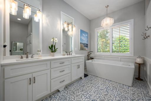Stunning 12x12 primary bathroom with double vanities, custom tile flooring, lighting, soaking tub, and walk-in tiled shower.
