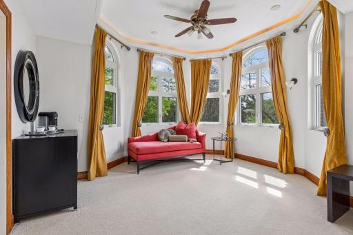 Two story lounge area in primary suite with bay windows and tray ceiling