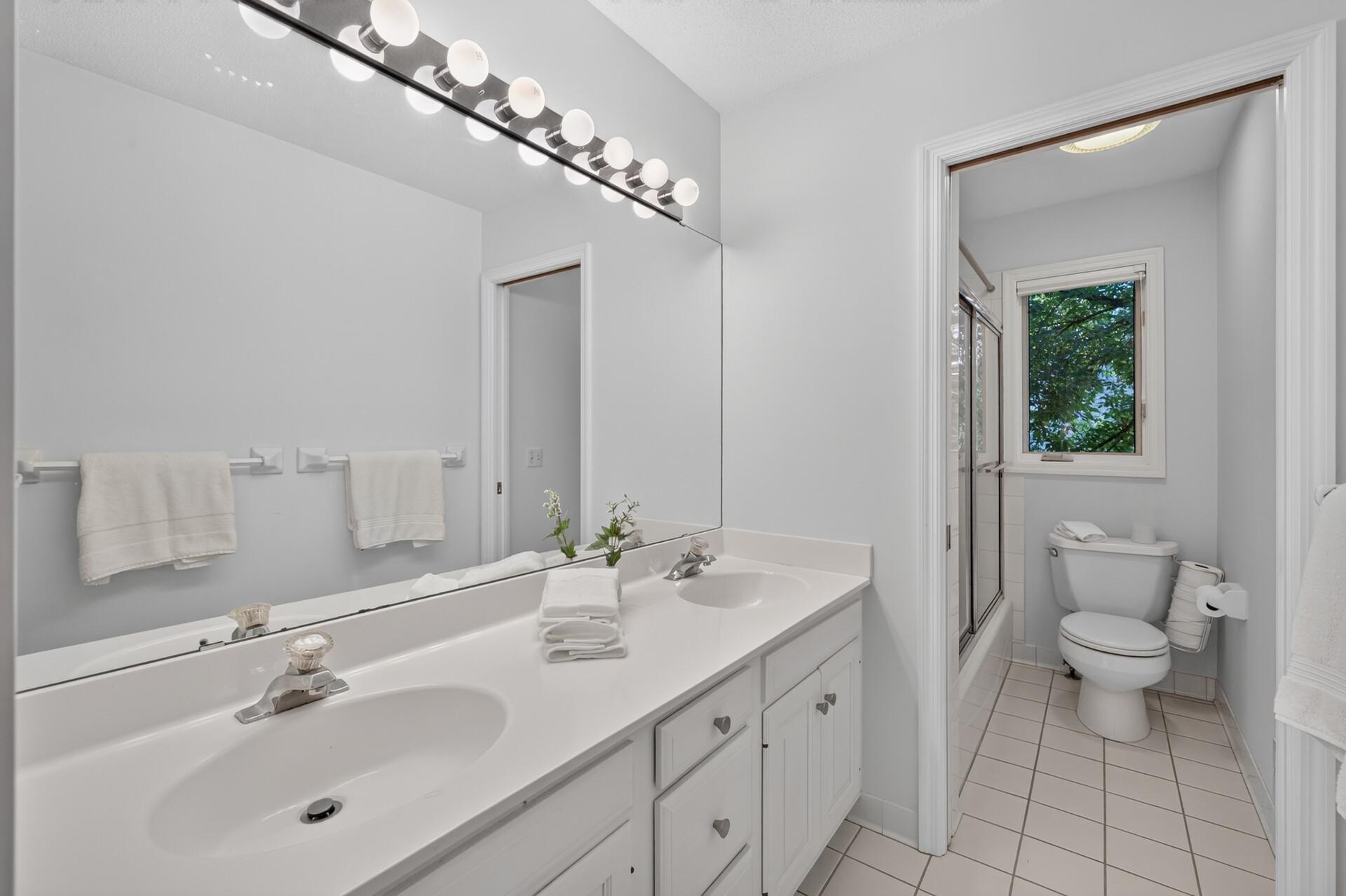 Full bath in hallway upstairs features double sinks and separated bath/toilet area.