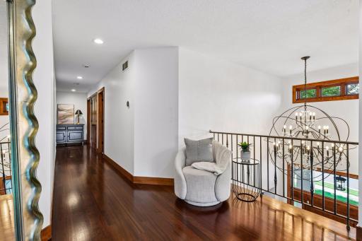 Upper-level gallery showcases a stunning statement chandelier, rich walnut-stained Brazilian Cherry hardwood floors, and open sightlines below. The thoughtfully designed layout provides seamless access to three spacious secondary bedrooms.