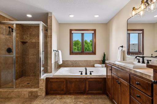 Indulge in a spa-inspired primary suite bath featuring a luxurious soaking tub, walk-in tiled shower, dual vanities, and rich custom cabinetry. Thoughtfully designed, upscale finishes and serene views. Private retreat offers everyday resort living.