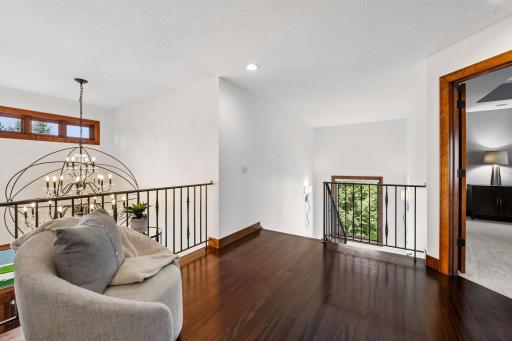 An impressive upper-level gallery showcases rich walnut-stained Brazilian Cherry hardwood floors, elegant iron railings, and dramatic sightlines below. Thoughtfully designed w/timeless craftsmanship, this space delivers architectural distinction.