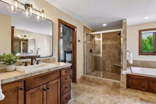 Primary suite bath featuring walk-in tiled shower, dual vanities, and rich custom cabinetry. Thoughtfully designed along with a walk in closet from the bathroom space.