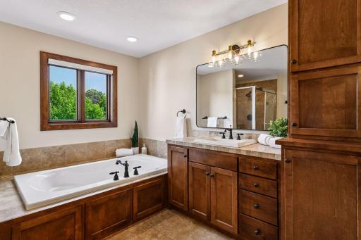 Indulge in a spa-inspired primary suite bath featuring a luxurious soaking tub, walk-in tiled shower, dual vanities, and rich custom cabinetry. Thoughtfully designed, upscale finishes and serene views. Private retreat offers everyday resort living.