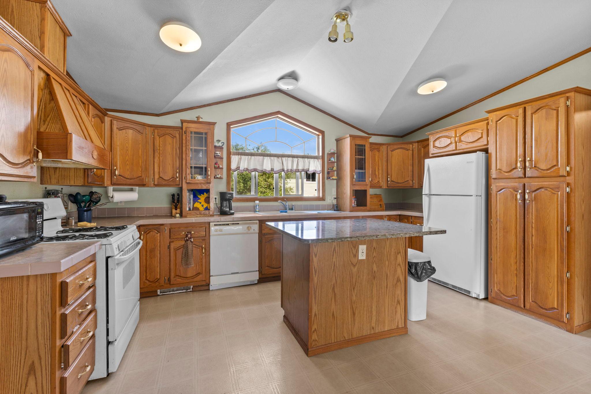 Spacious kitchen with tall ceilings, large window, gas stove and ornate vent-hood