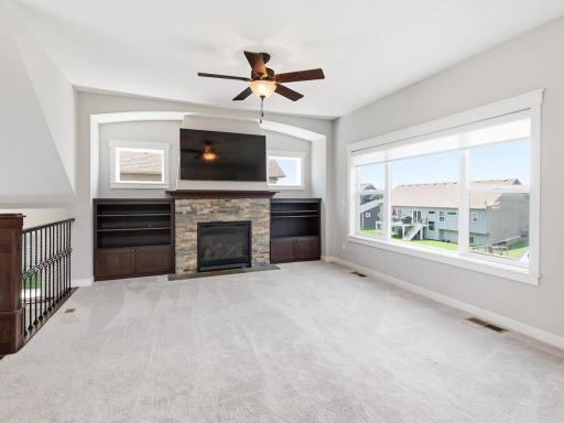 Spacious living room featuring a stunning stone fireplace with a custom-built-in entertainment center, large windows flooding the space with natural light, and elegant architectural details.