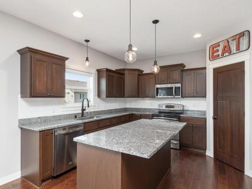 Well-appointed kitchen with quality finishes including granite counters, tile backsplash, center island with seating, and modern lighting fixtures.