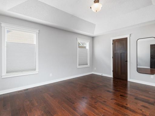 Bright and spacious primary bedroom with large windows, tray vault ceiling, and rich hardwood flooring.