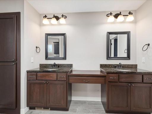 Luxurious primary bathroom with dual vanities, granite countertops, custom cabinetry, framed mirrors, and designer lighting fixtures.