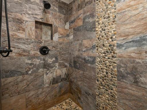 Spa-like walk-in shower featuring stunning floor-to-ceiling tile work, decorative pebble accent wall, built-in niche, and modern fixtures.