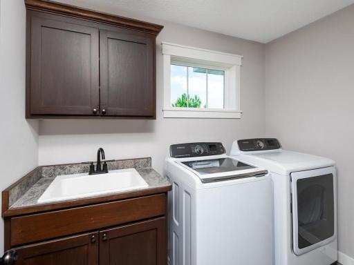 Convenient upper-level laundry room with granite countertop, utility sink, custom cabinetry, and space for a full-size washer and dryer.