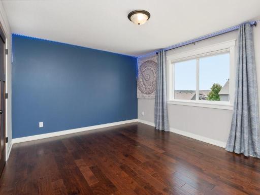 Spacious bedroom with designer blue accent wall, hardwood flooring, large windows with custom window treatments, and excellent natural light.