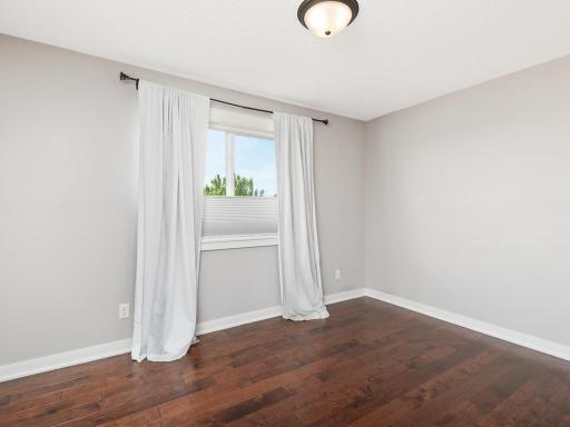 Spacious guest bedroom with hardwood flooring, neutral paint colors, and beautiful natural light.