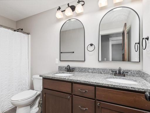 Stylish full bathroom with dual vanities, granite countertops, custom cabinetry, designer mirrors, and tub/shower combination with tile surround.