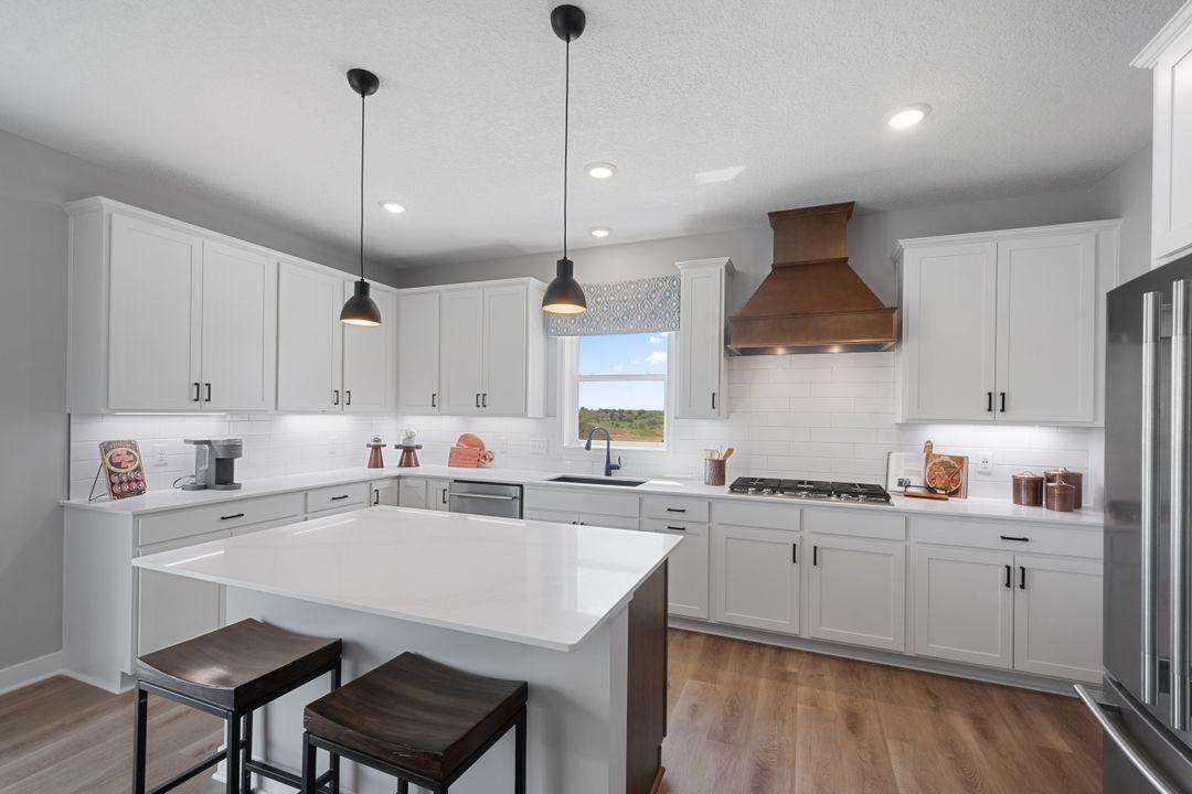 Enjoy your exceptional gourmet kitchen with a 5-burner gas cooktop, wood vent hood, tile backsplash, and a center island with seating and storage. Photo of model, colors and finishes may vary.