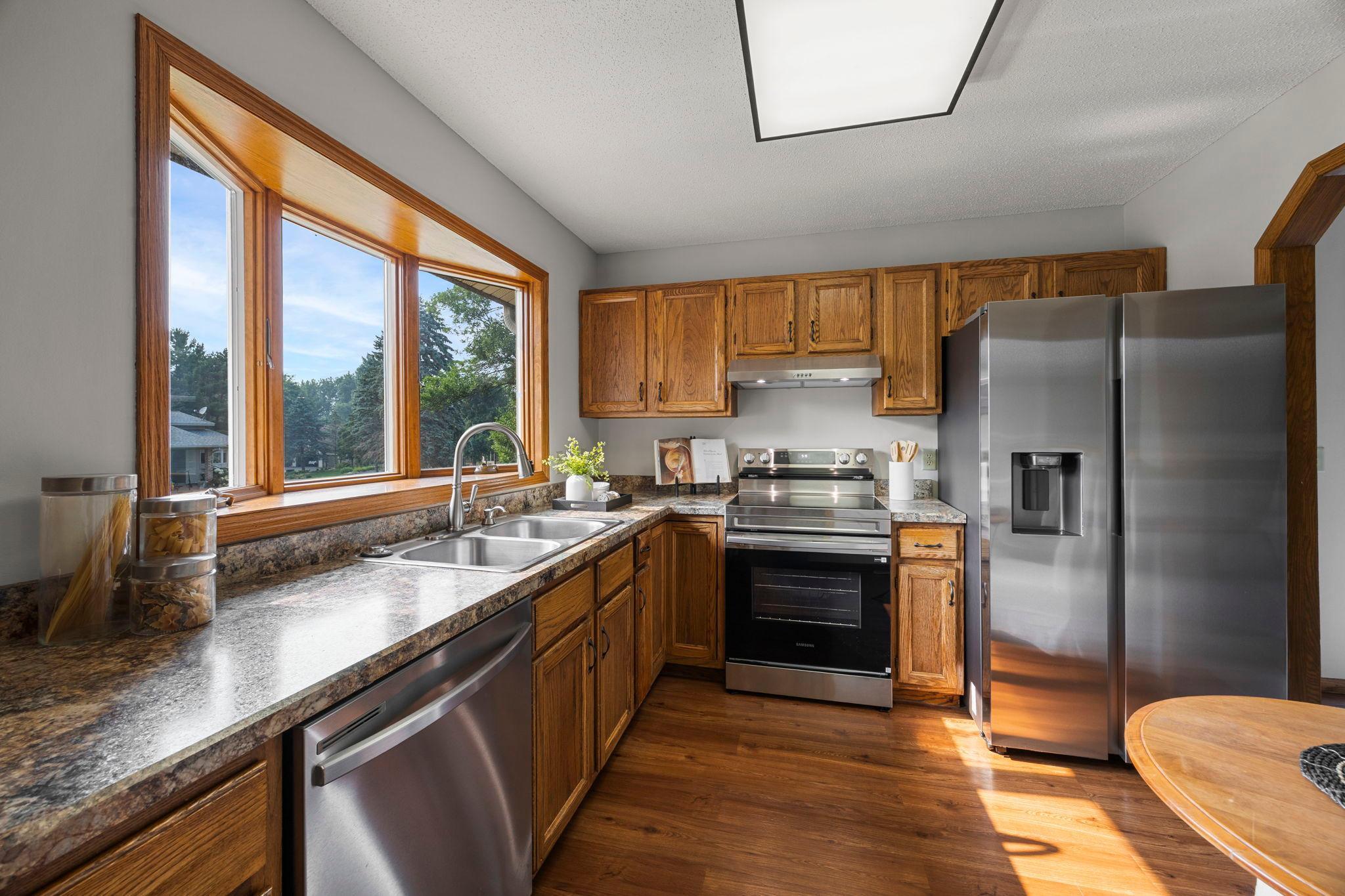 The kitchen features brand-new stainless steel appliances, ample wood cabinetry, generous counter space, and a large front-facing window above the sink offering peaceful neighborhood views.