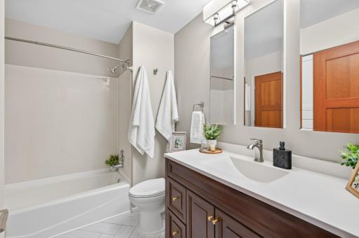 Upper level full bathroom with tub and shower combination, quartz-topped vanity and updated finishes. with built-in storage cabinet.