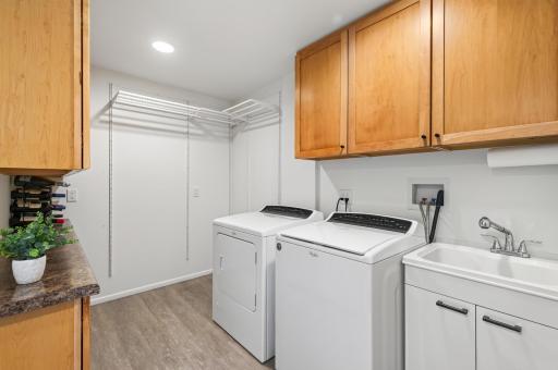 Spacious laundry room with washer and dryer, utility sink, abundant cabinetry, counter space and hanging storage.