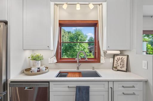 Large kitchen window brings in natural light above the sink, with quartz countertops, white cabinetry and stainless steel dishwasher.