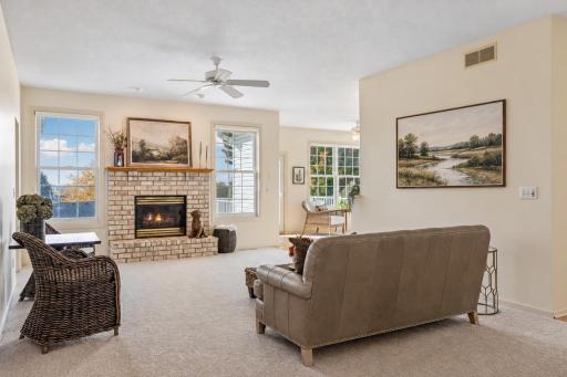 A brick fireplace and tall windows create a comfortable, bright living room. Wall artwork virtually added.