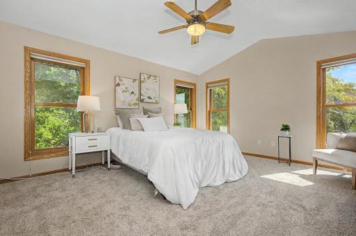 A spacious primary retreat with vaulted ceilings, treetop views, and natural light streaming in from every direction.