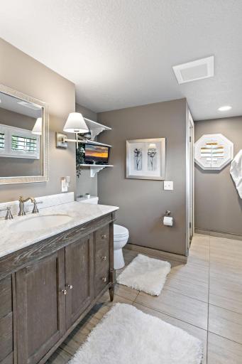 A stylish primary bath with marble-topped vanity, wood cabinetry, and walk-in shower access