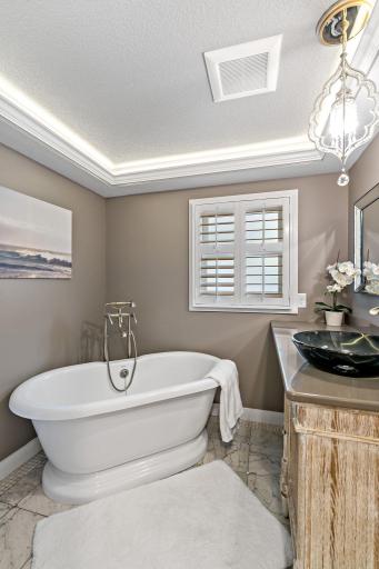 A spa-worthy bath — freestanding soaking tub, glass vessel sink, and a glowing tray ceiling set the tone for relaxation