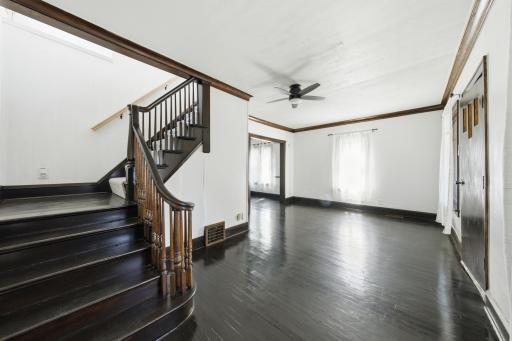 Through living room around to formal dining room! Gorgeous oak banister, 9 ft. ceilings, coved corners, gleaming maple floors, a lighted ceiling fan, and new curtains and curtain rods!
