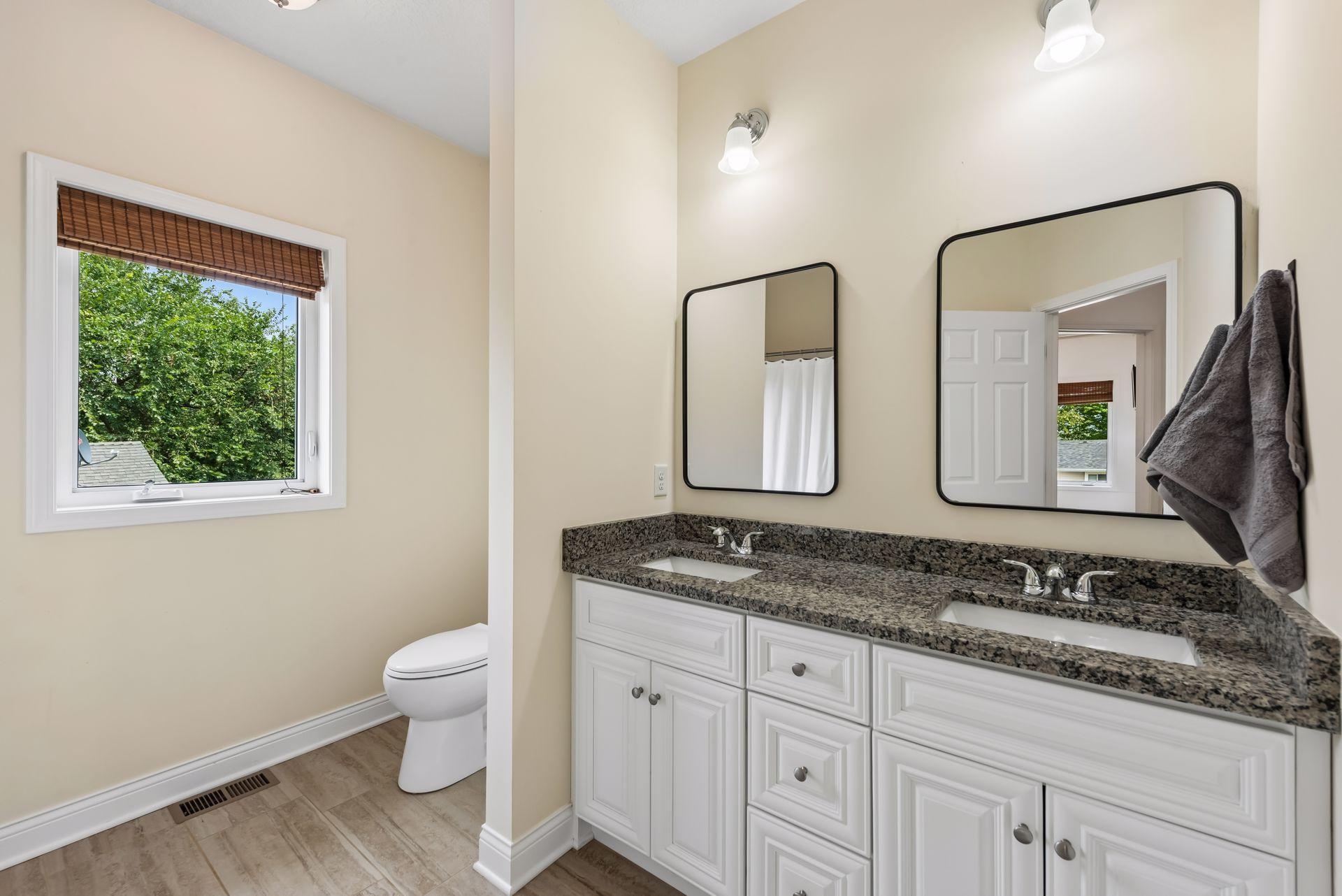 A spacious dual-sink vanity with granite countertops provides convenience for busy mornings, while the thoughtful layout offers privacy between the vanity and bath area.
