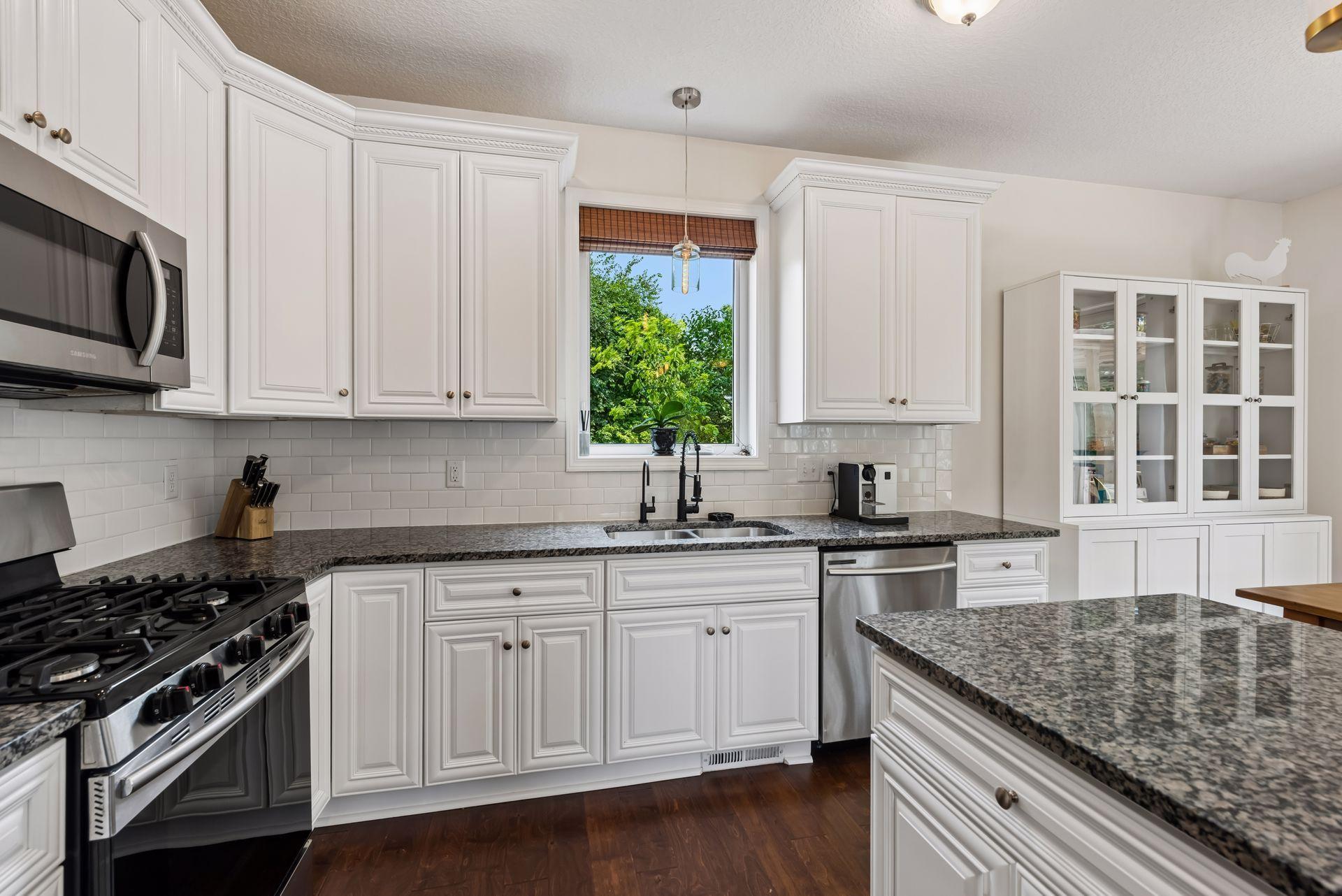 Beautiful white cabinetry, granite countertops, subway tile backsplash, and a large picture window create a bright, functional kitchen with timeless appeal and generous prep space for every meal.