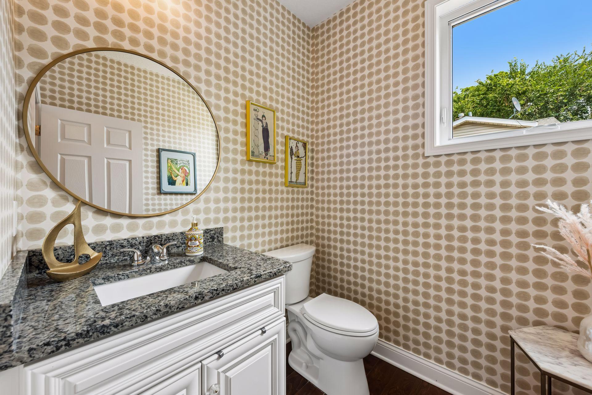 This charming powder room features granite countertops, elegant cabinetry, designer wallpaper, and a bright window that fills the space with natural light and character.