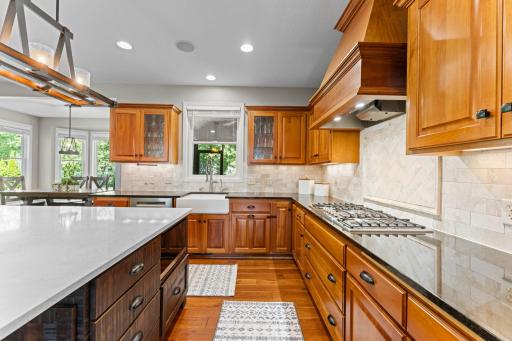The kitchen includes a window over the white ceramic apron sink. It also includes stainless steel appliances: an LG refrigerator, a double Bosch wall oven with convection, a dishwasher, & a 5-burner gas stove with an exhaust hood.