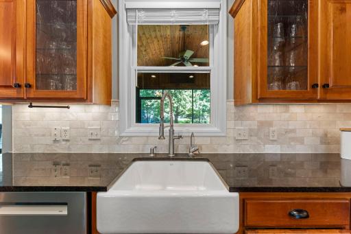 View of the kitchen window looking into the screened porch, apron sink with disposal, pull-down faucet and beautiful tile backsplash.