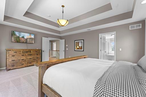 This view of the primary bedroom showcases the multi-level tray ceiling, paneled French doors and the private full bathroom.