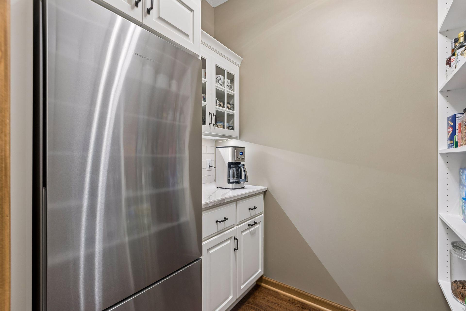 Convenient walk-in pantry near the kitchen featuring custom cabinetry and a full-size refrigerator/freezer.