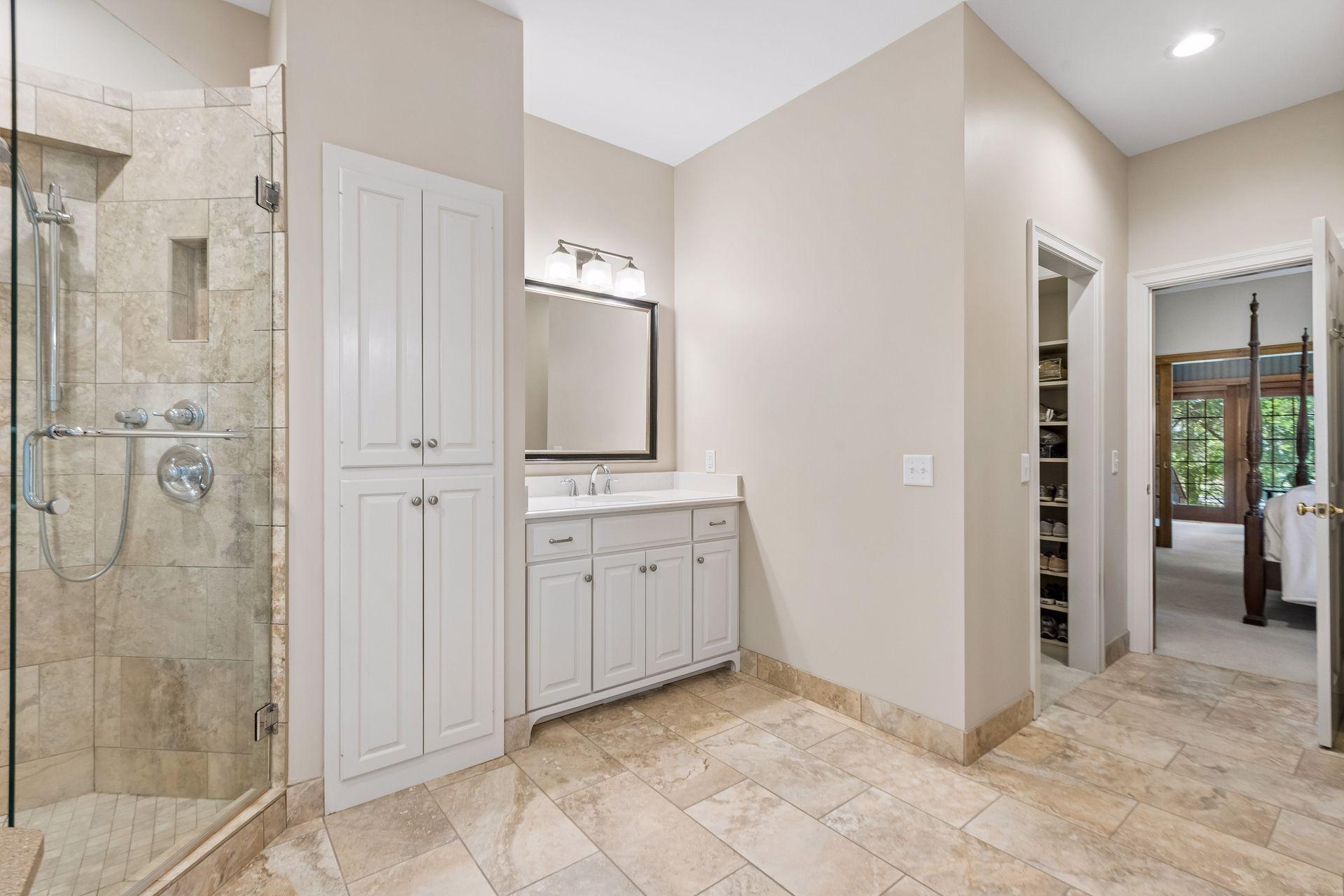 This photo highlights the tile shower, one of the vanities, one of the two walk-in closets, and access to the primary bedroom.