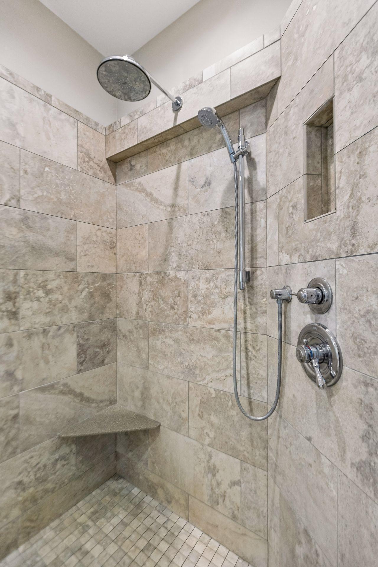 Updated tile shower in the primary bath with the convenience of a handheld shower head and a built-in bench.